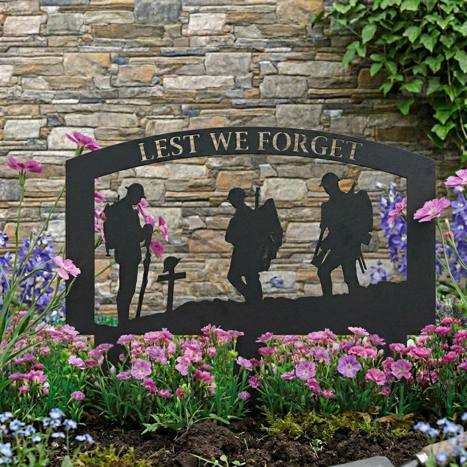 Decorative garden sign with silhouettes of soldiers and 'Lest We Forget' text, surrounded by flowers and a stone wall.