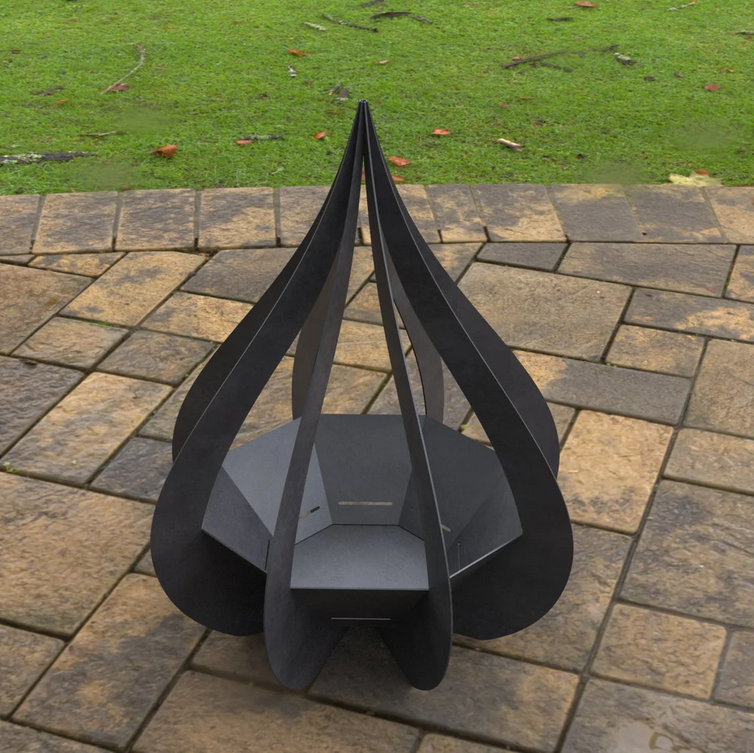 Black metal fire pit on a stone patio with grass in the background