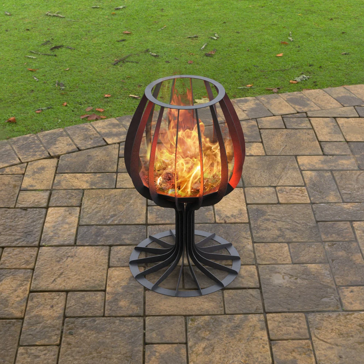 Metal fire pit on a paved patio with grass in the background