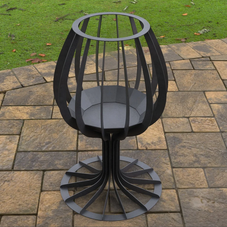 Black metal outdoor fire pit on a paved patio with grass in the background